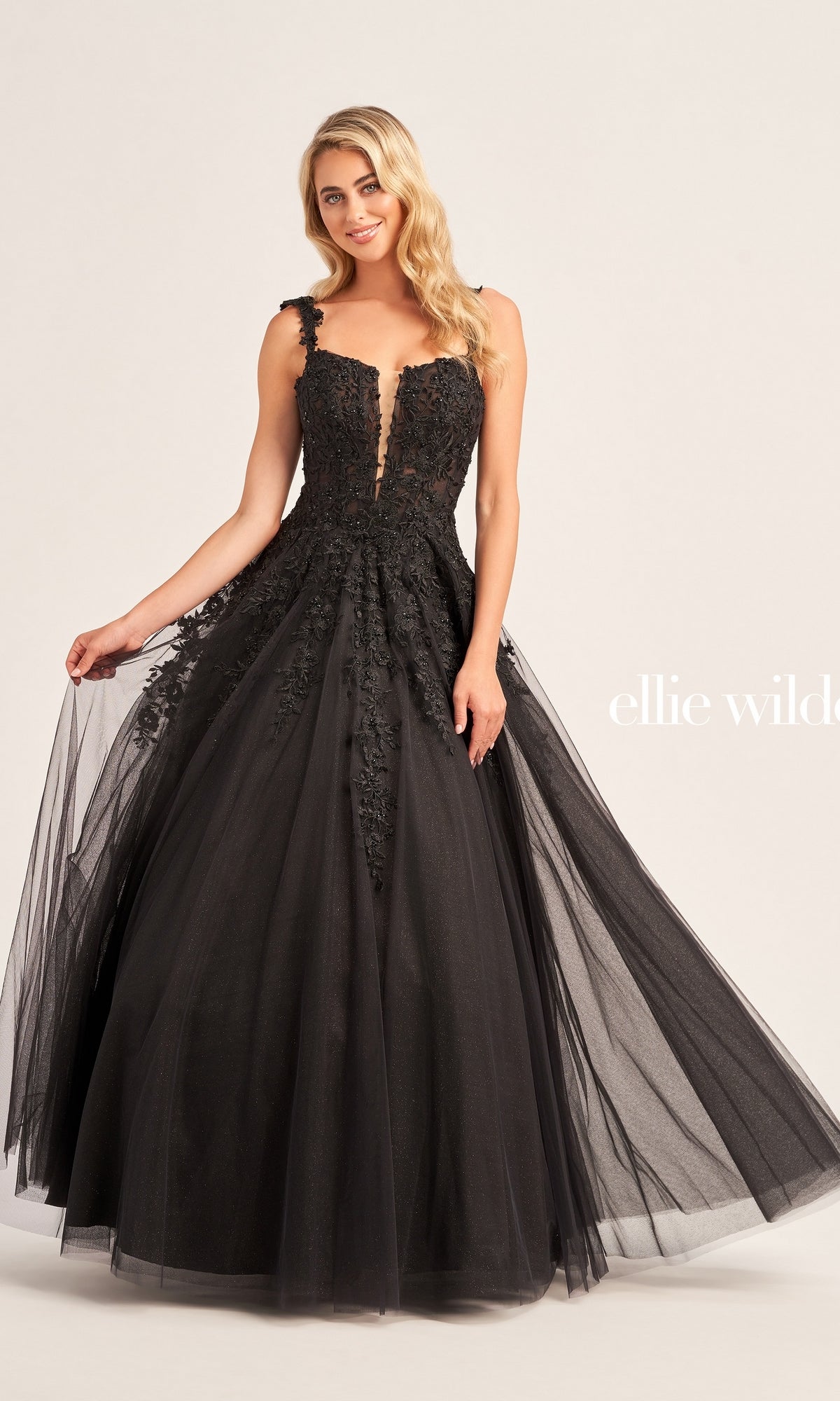 A woman poses against a plain background in the Ellie Wilde EW120014 Long Glitter Prom Ball Gown, a sleeveless, floor-length black dress featuring floral lace details and a glitter tulle skirt.